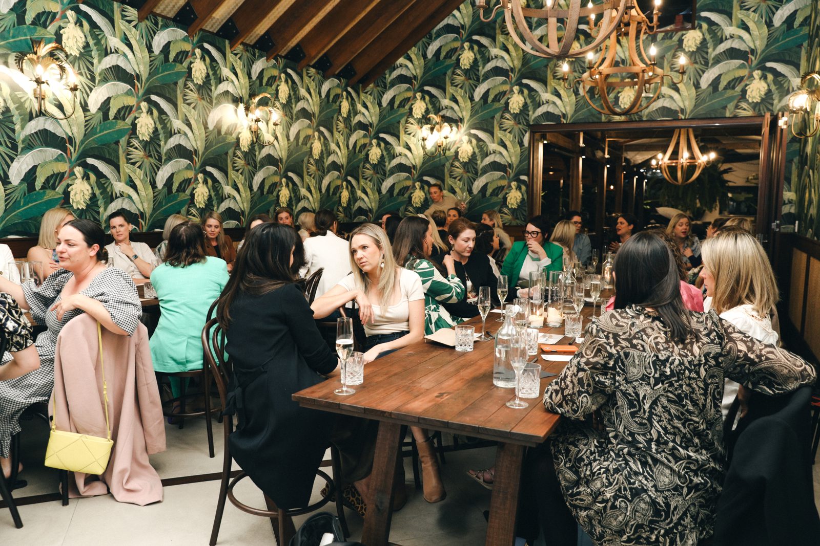 Guests talking at long tables in a tropical-wallpapered dining room