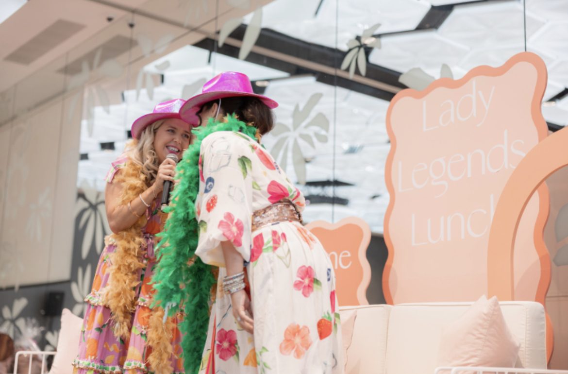 Hosts in pink cowboy hats on stage at the Lady Legends Lunch